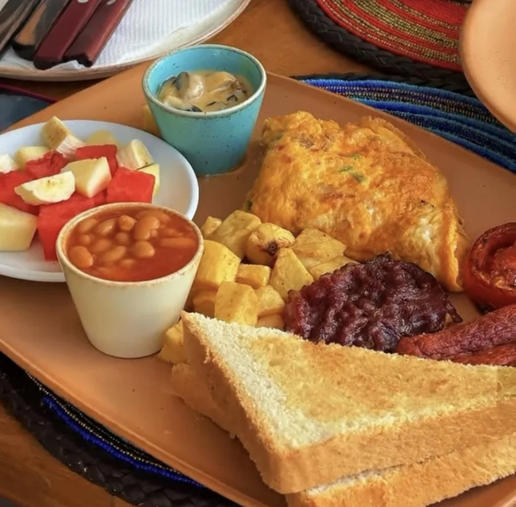 A full breakfast plate with omelette, sautéed potatoes, baked beans, toast and fresh fruit