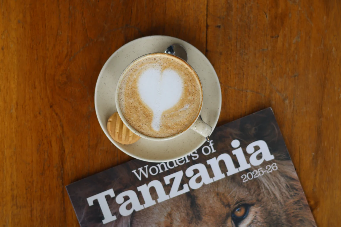 A cappuccino with heart latte art beside a Wonders of Tanzania magazine